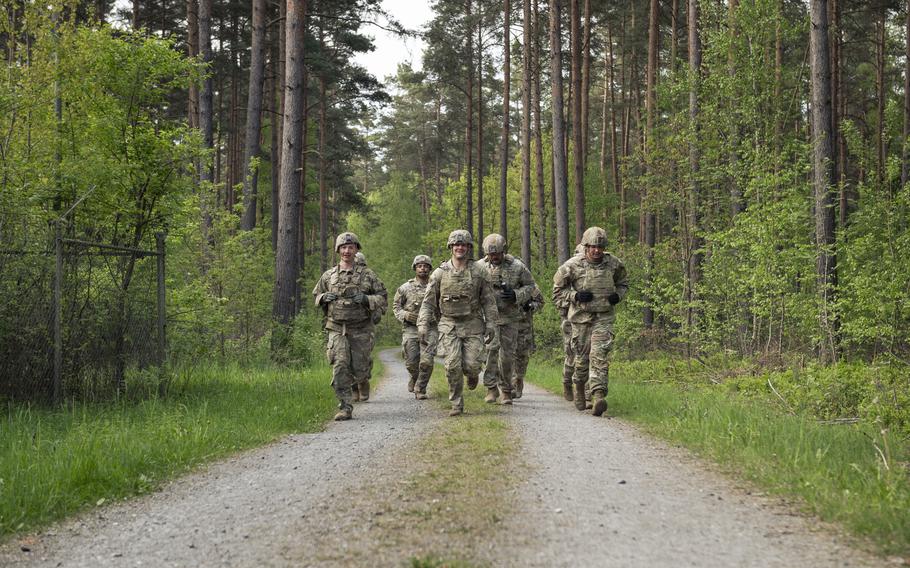 A team of soldiers is seen jogging on a dirt road in a forest.