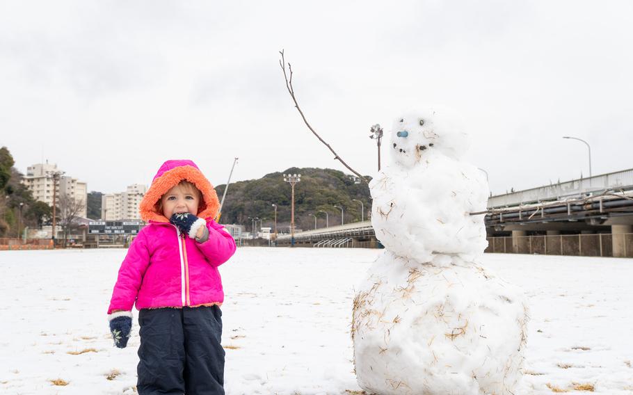 A child poses with a snowman at the Ikego housing detachment near Yokosuka Naval Base, Japan, Tuesday, Feb. 6, 2024.