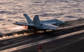 A military fighter jet speeds down the flight line as it takes off from an aircraft carrier at sea.