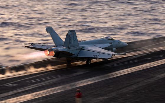 A military fighter jet speeds down the flight line as it takes off from an aircraft carrier at sea.
