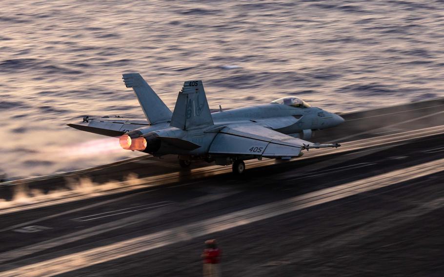 A military fighter jet speeds down the flight line as it takes off from an aircraft carrier at sea.