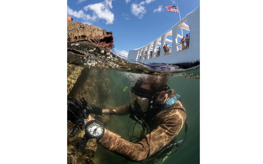 A diver in scuba gear is seen just below the surface of water next to the wreckage of a ship, with the sky above the waterline at the top of the scene.