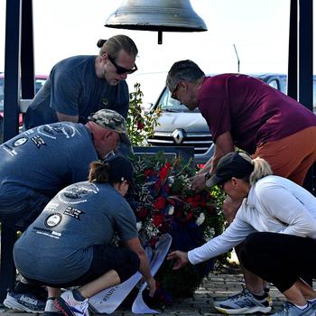 Five people bend over to lay a wreath below a bell.