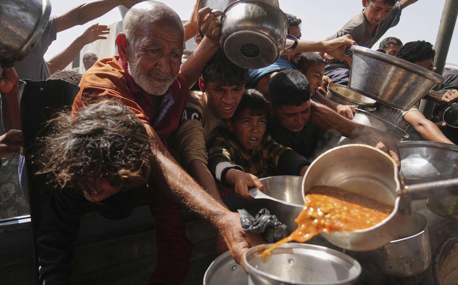 People, most prominently an older man and several young boys, reach pots and pans out trying to get food.