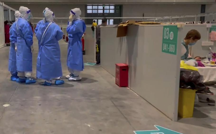 In this image taken from video provided by Beibei, who asked to be identified only by her given name, medical workers wearing protective suits chat as a resident takes a rest at the National Exhibition and Convention Center on April 15, 2022, in Shanghai.  The convention center converted to a quarantine facility set up for people who tested positive but have few or no symptoms. 