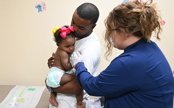 A man holds a baby in a diaper while a nurse administers a shot in the baby’s arm.