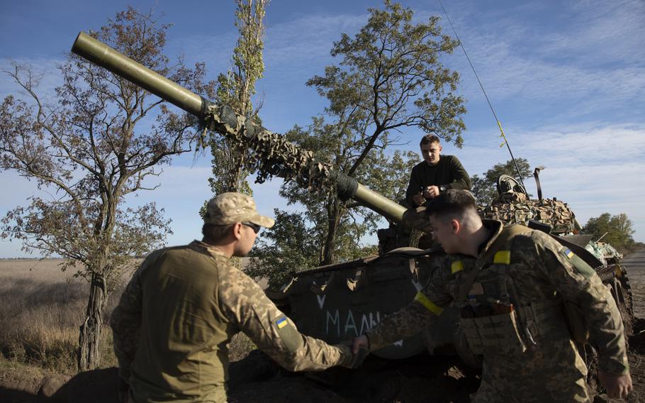 Ukrainian soldiers greet one another by a Russian tank along a road in the Kherson region of southern Ukraine on Thursday. M