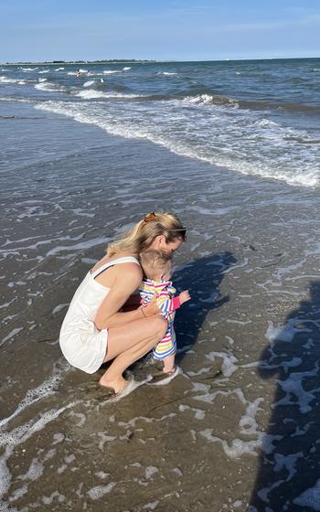 A woman and a child stand in shallow water on a beach.