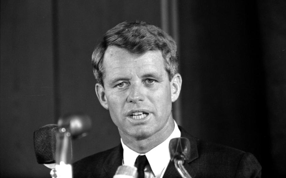 A black and white photo of Robert F. Kennedy, seen from the shoulders up with microphones in front of him.