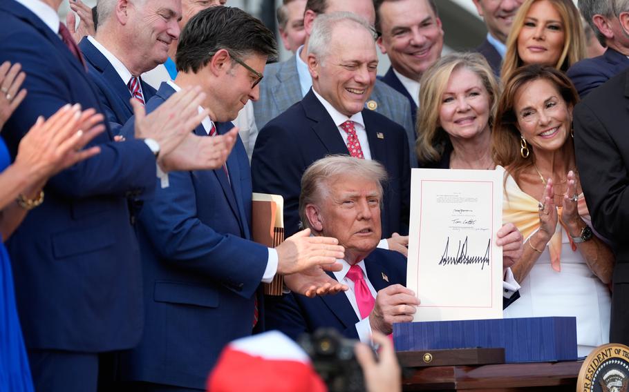 Trump, with members of congress and other onlookers applauding, holds up the law showing his signature.