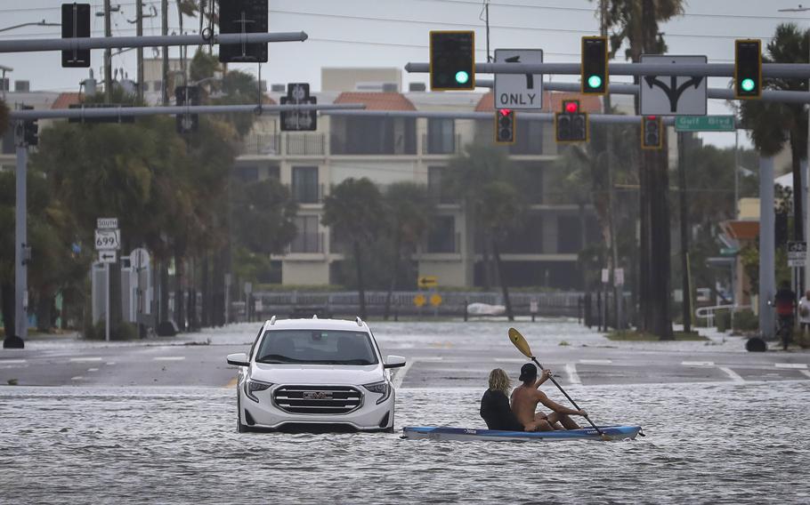 A man and woman kayak past an abandoned vehicle in the intersection of Boca Ciega Drive and Pasadena Avenue in St. Pete Beach, Florida. 