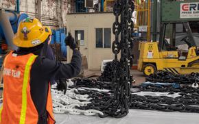 Norfolk Naval Shipyard workers move an anchor chain into position for cleaning and repair.