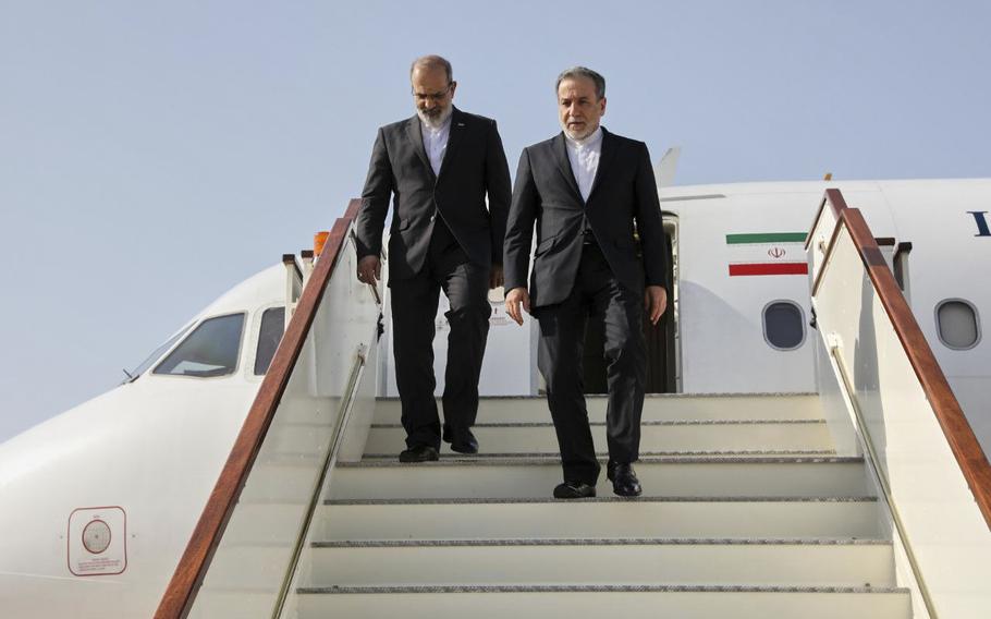 Two men in suits walk down the stairs of an airplane.