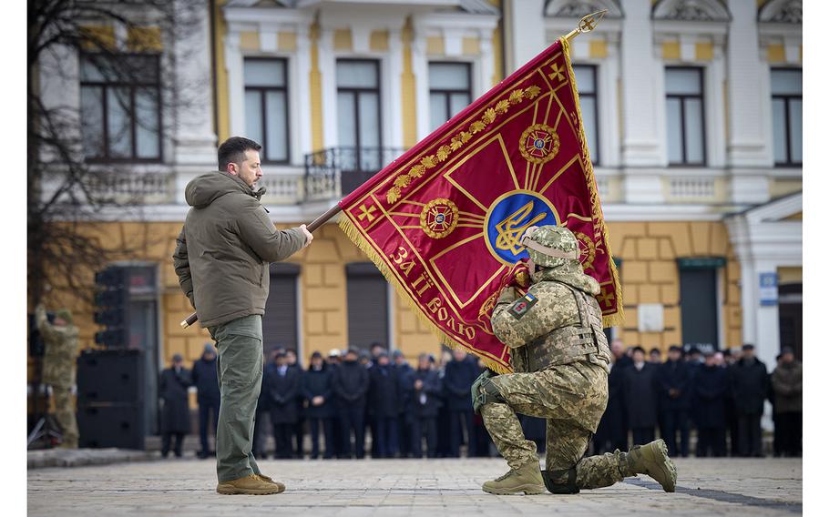 Ukrainian President Volodymyr Zelenskyy, left, holds the flag of a military unit as an officer kisses it, during commemorative event on the occasion of the Russia Ukraine war one year anniversary in Kyiv, Ukraine, Friday, Feb. 24, 2023. (Ukrainian Presidential Press Office via AP)