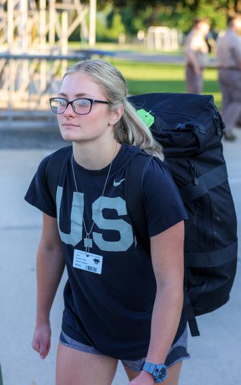A cadet with a shirt that says U.S. and a backpack walks on campus.