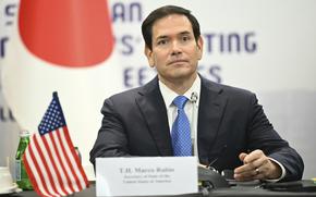 Marco Rubio sits at a conference table next to a small U.S. flag, with a larger Japanese flag behind him.