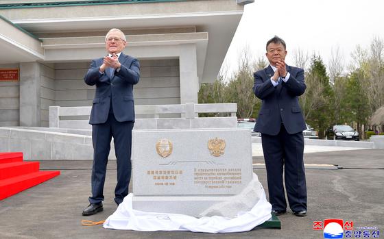 Two men standing next to a gray-white block and clapping.