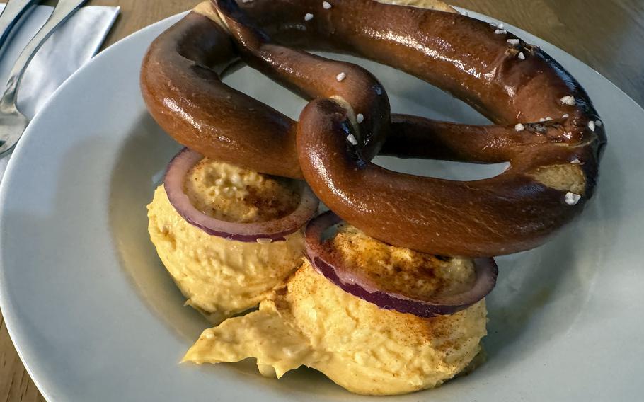 A pretzel on top of two scoops of spreadable cheese and sliced onions.