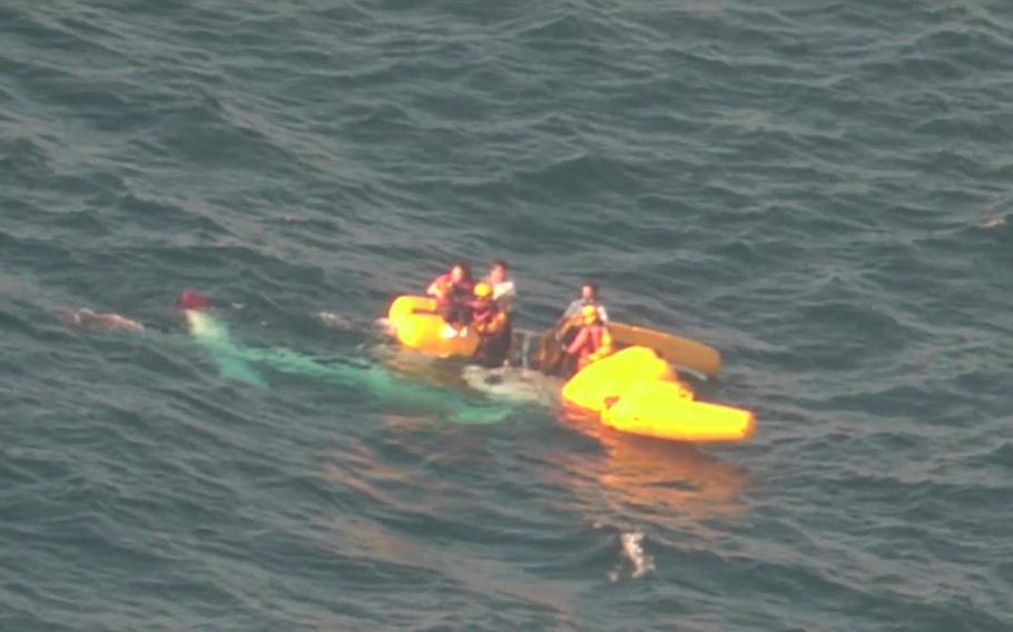 Rescuers work near people aboard a medical transport helicopter after it fell into the sea.