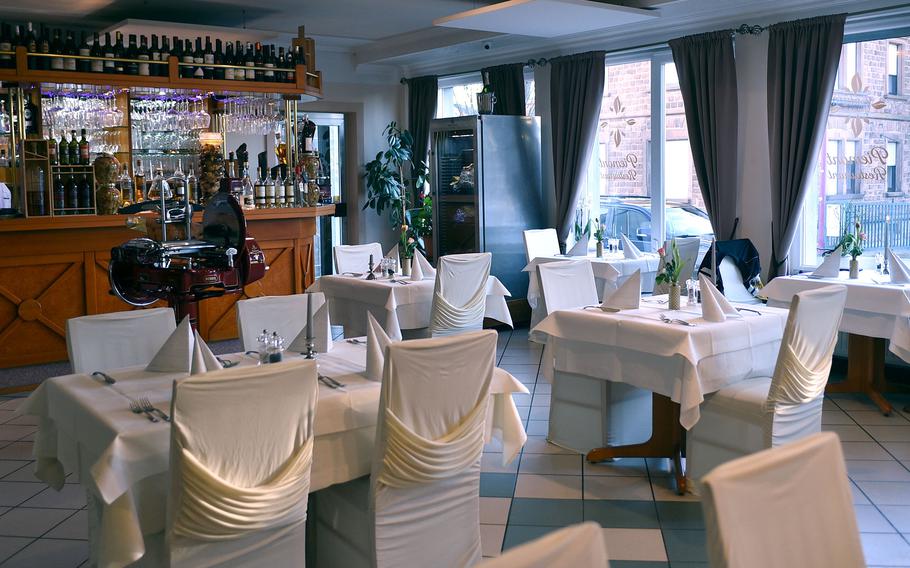 A dining room with white chairs and tablecloths, and a wooden bar in the background.
