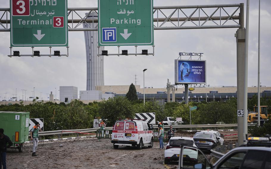 Vehicles at the site of a missile strike, with road signs overhead and the air traffic control tower in the background.