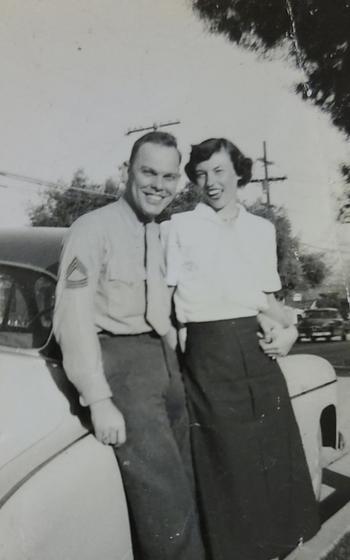 A Marine and a woman pose for a picture together by a car.