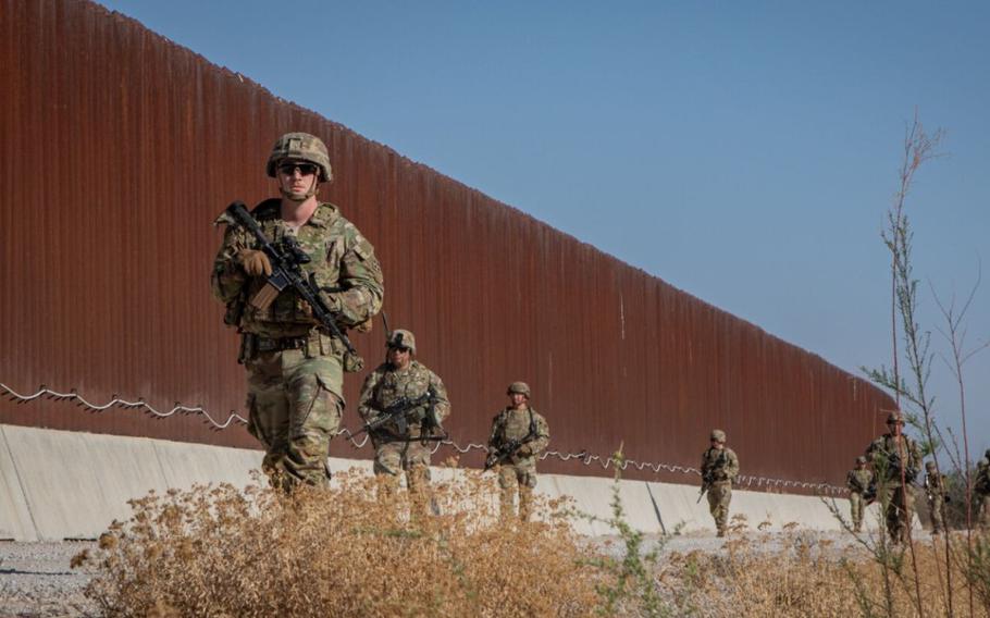 A group of soldiers walks along the southern border wall. 
