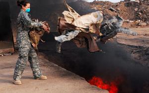 Senior Airman Frances Gavalis, a 332nd Expeditionary Logistics Readiness Squadron equipment manager, tosses unserviceable uniform items into a burn pit in Balad, Iraq, in 2008.