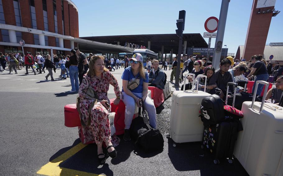 Stranded passengers sit on luggage while waiting outside a train station in Madrid.