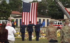 Service members salute after placing a wreath in front of hundreds of firefighters' helmets and protective clothing at a ceremony at Ramstein Air Base, Sept. 10, 2021, to mark the 20th anniversary of the attacks of 9/11 