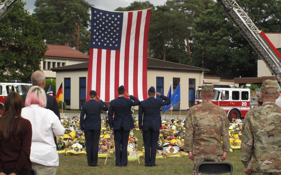 Service members salute after placing a wreath in front of hundreds of firefighters' helmets and pieces of protective gear at a ceremony at Ramstein Air Base, Sept. 10, 2021, to mark the 20th anniversary of the attacks of 9/11.