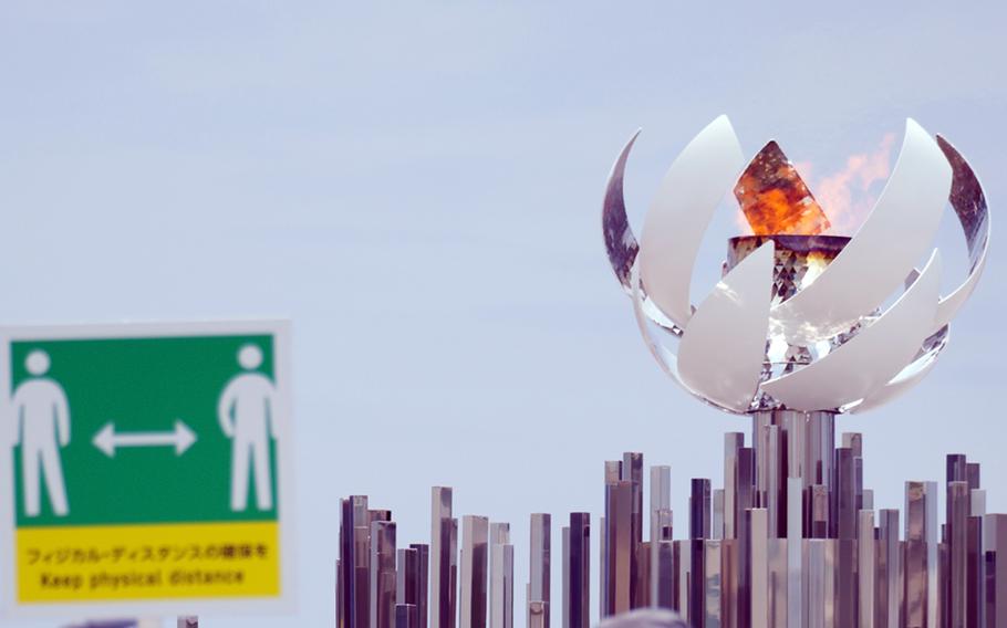 A sign reminds people to practice social distancing when visiting the Olympic cauldron near Ariake, Tokyo, July 30, 2021. 