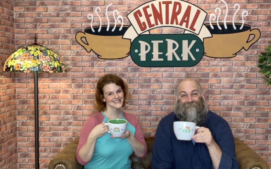 Ann Pinson and Chad Garland pretend to grab cups of joe on a loose replica of the ''Friends'' coffee shop set Oct. 21, 2021. It is one of nearly two dozen sets and backdrops at SnapMySelf, a ''selfie museum'' in downtown Kaiserslautern, Germany.