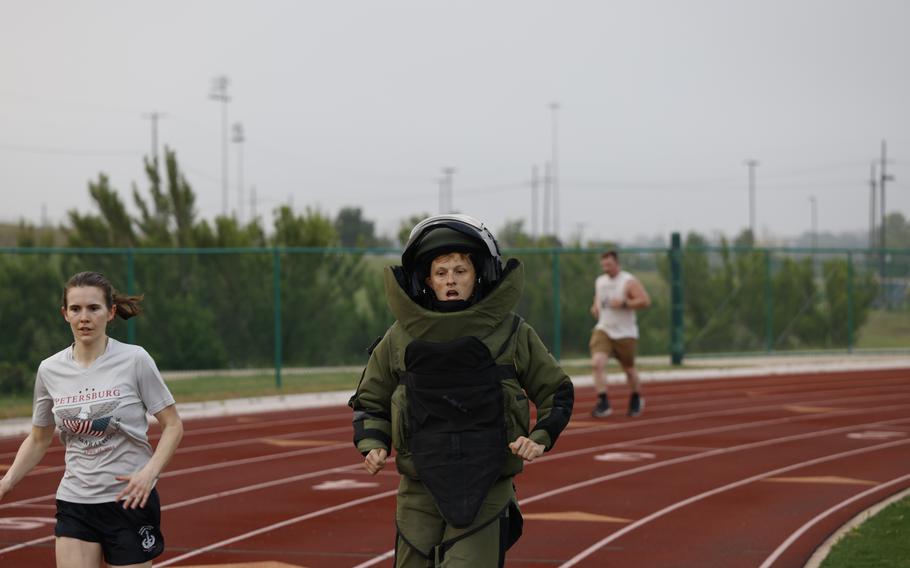 A man running in a bomb suit seen from the legs up, with two others running near him.