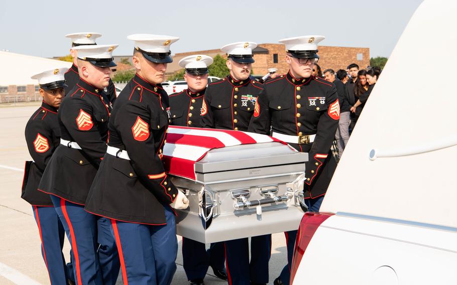 Marines in uniform carry a casket draped in an American flag.