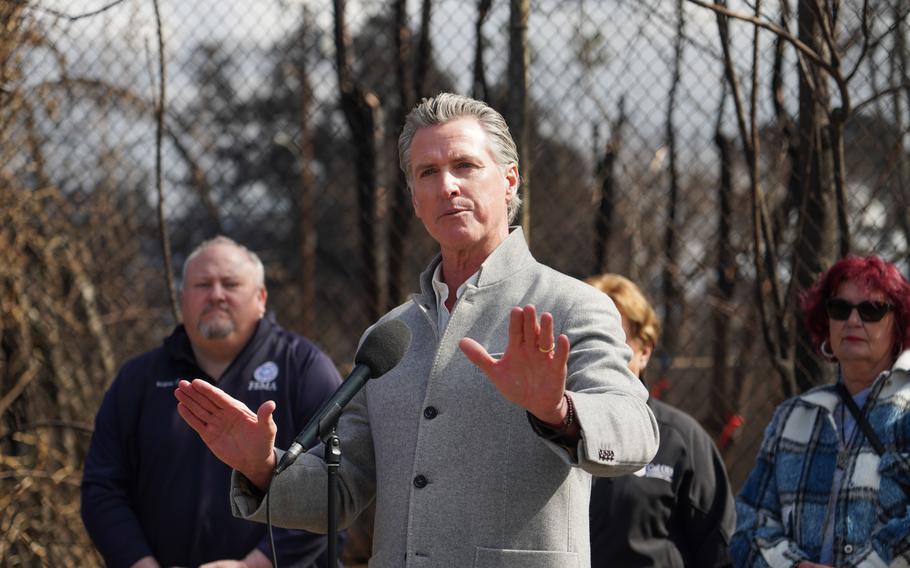 California Governor Gavin Newsom gestures as he speaks through a microphone.