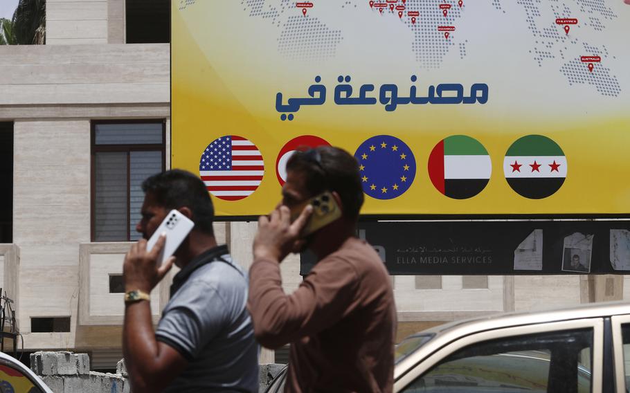 Syrian men speak in front of a sign with the flags of other countries.
