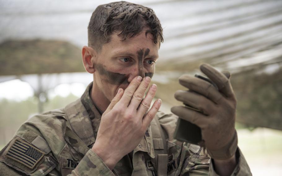 A soldier applies camouflage paint while looking at a handheld mirror.