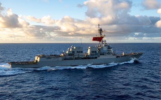 A military ship transits through open water with clouds above the horizon in the background.