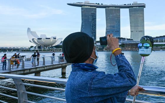 A man takes pictures of a mask wearing a face mask in front of the Marina Bay Sands hotel and resort in Singapore on Feb. 18, 2022,. Governments across Southeast Asia are bringing back measures to limit a rapid resurgence of respiratory infections. (Roslan Rahman/AFP/Getty Images/TNS)