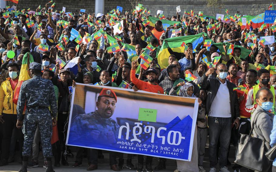 People gather behind a placard showing Prime Minister Abiy Ahmed at a rally organized by local authorities to show support for the Ethiopian National Defense Force (ENDF), at Meskel square in downtown Addis Ababa, Ethiopia, Sunday, Nov. 7, 2021. Placard in Amharic reads: “We Have Respect For Our Brave National Army.” Ethiopia’s prime minister says he will lead his country’s army “from the battlefront” beginning Tuesday, Nov. 23, 2021.