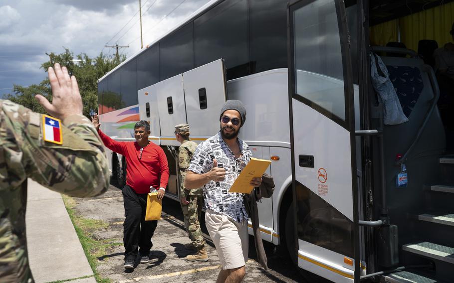 Migrants wave goodbye to the National Guard as they board a D.C.-bound bus outside of the Val Verde Border Humanitarian Coalition in Del Rio, Tex., on Aug. 11, 2022.