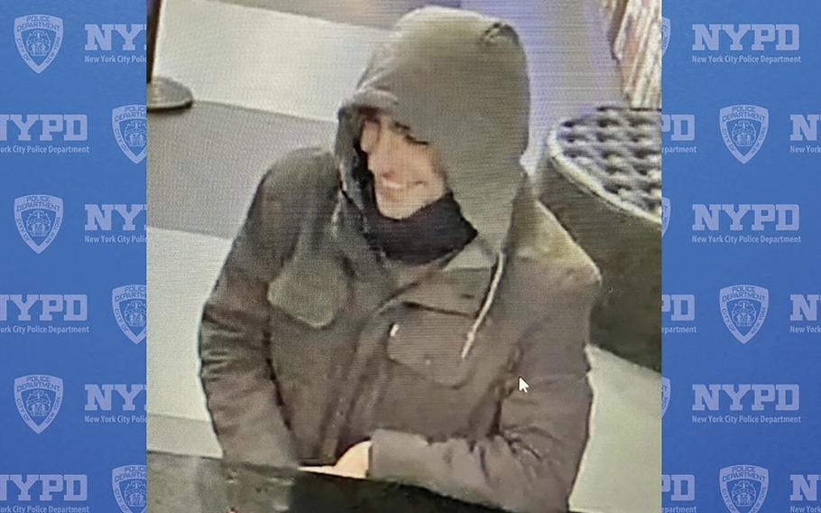 Security camera footage of a man standing at a counter wearing a coat with the hood pulled over his head.