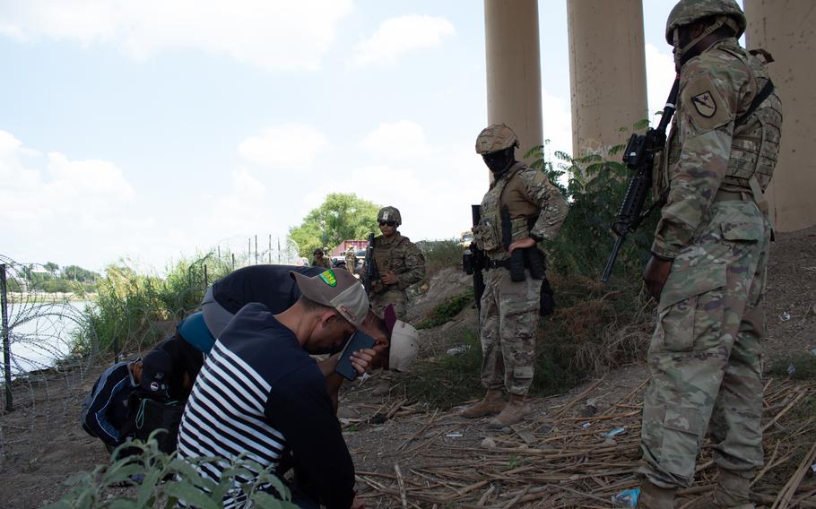 Texas National Guard troops watch over migrants who illegally crossed the Rio Grande from Mexico into Texas beneath the Camino Real International Bridge in Eagle Pass, Texas, in an undated photo. The soldiers then led the migrants to a U.S. Customs and Border Protection processing center. 