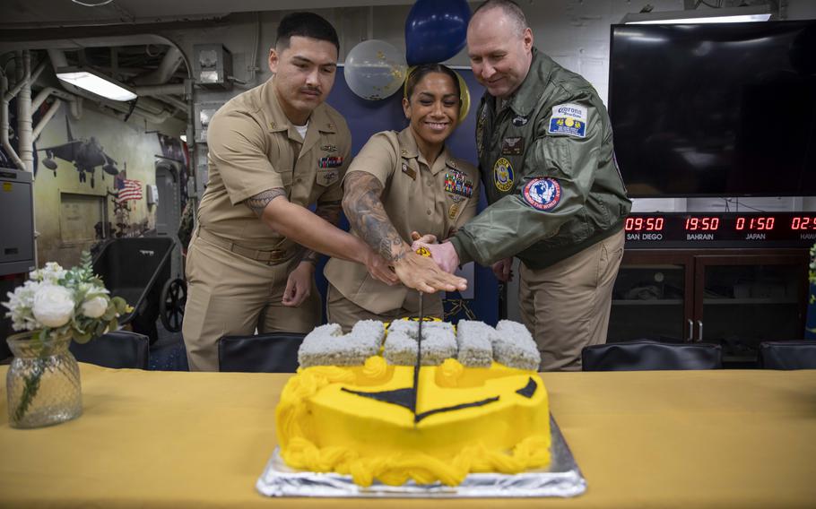 Three sailors cut a yellow cake together that says “USN”