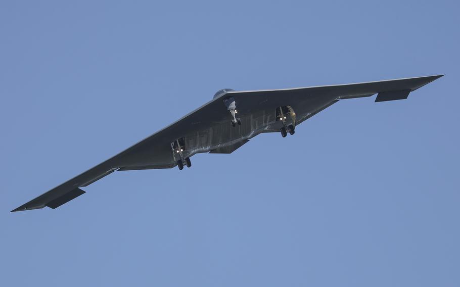 A stealthy B-2 bomber airborne, with a blue sky in the background.
