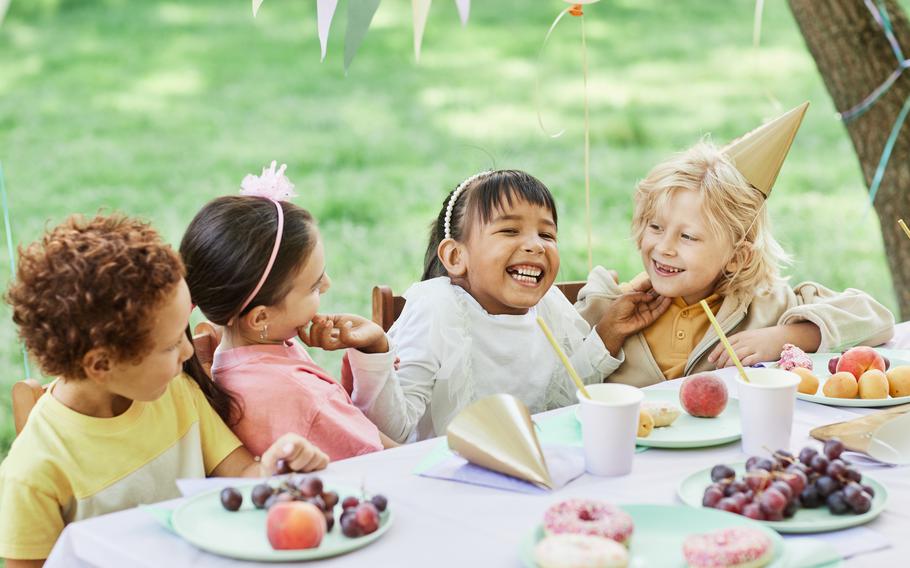 Portrait of smiling little girl with friends at picnic table outdoors enjoying Birthday party in Summer