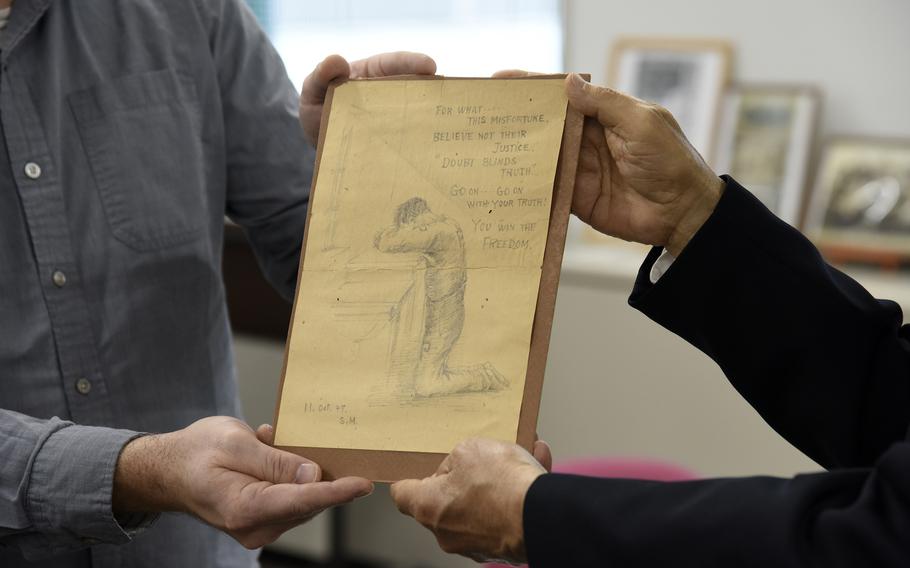 Philip Ackland, left, a Department of Defense Education Activity teacher at Yokosuka Naval Base, Japan, presents a sketch Shichiro Matake made at Sugamo Prison to the former inmate's son, Kiyoshi Matake, at Kurume University in Fukuoka, Japan, Nov. 24, 2023. 