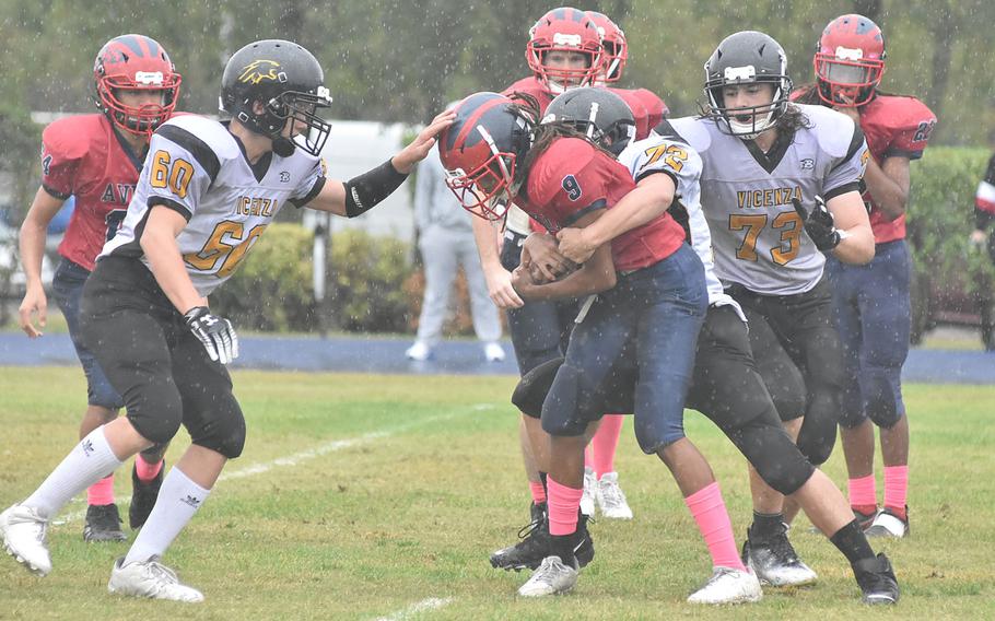 Aviano quarterback Andrew Walker tries to hold onto the ball during a steady rain as Vicenza's Kaden Peterson grabs him from behind and Ian Rhynalds approaches in the Saints' 40-0 victory on Saturday, Oct. 22, 2022.
