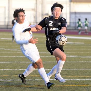 E.J. King’s Amin Alipourkashki and Zama‘s Keahnu Araki chase the ball. The Trojans and Cobras played to a 1-1 draw Friday in the Perry Cup.